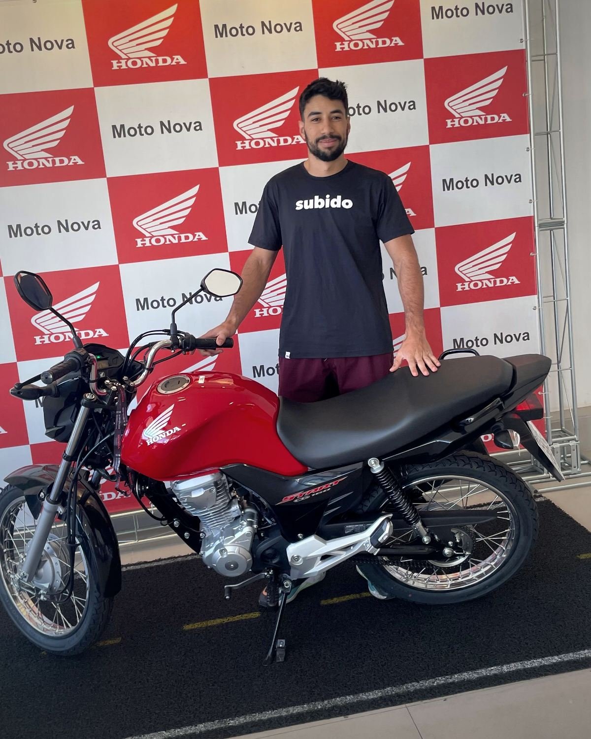 João Jorge ao lado da primeira moto, uma Honda Start 160 vermelha, na concessionária